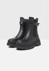 Bottines en cuir noir avec une semelle plate-forme épaisse, fermeture éclair sur le côté et panneaux élastiques sur les côtés. Présente une boucle en métal décorative sur la sangle.