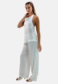 Top in seta bianca senza maniche con un design fluido abbinato a pantaloni bianchi a gamba larga, caratterizzati da una texture liscia e uno stile minimalista.