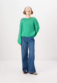 Grøn strikket sweater med brede ærmer, parret med højttaljede blå jeans. Modellen har dyreprint slip-ons og mønstrede ørevarmere på.
