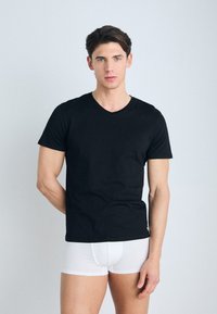 Zwarte katoenen t-shirt met korte mouwen en een V-hals ontwerp, gedragen over witte boxershorts. Eenvoudige en aansluitende stijl.