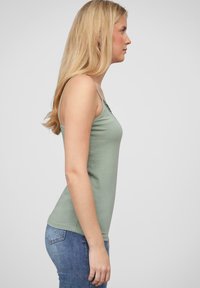 Mintgrønn tank top med tynne stropper, tettsittende design og rund utringning, parret med blå denimjeans. Glatt bomullsmateriale.
