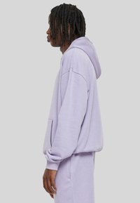 Helle lila Kapuzenpullover aus weichem Stoff, mit einer großen Kapuze, Fronttasche und lockerer Passform. Kombiniert mit passenden Sweatpants.