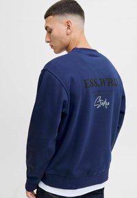 Navy sweatshirt with crew neck, soft texture, and black printed text on the back, including "ESS.WRD." and "Studio." Classic design.