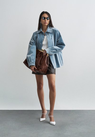 Džínsová bunda světle modré barvy, bílý žebrovaný top, černá minisukně, velké hnědé psaníčko a bílé špičaté podpatky na neutrálním pozadí.