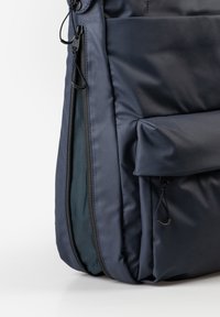 Marineblauer Rucksack aus strukturiertem Stoff, mit einem Reißverschlussfach und einem umklappbaren Deckel mit zusätzlichen Taschen.