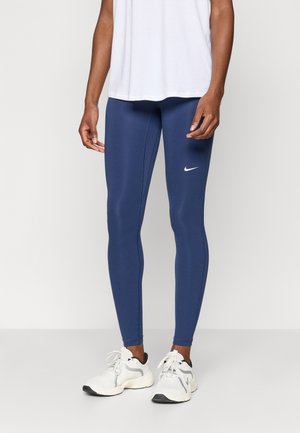 Granatowe legginsy wykonane z elastycznego materiału, o dopasowanym kroju i małym białym logo Nike na górnej części uda. Noszone z białymi butami sportowymi.