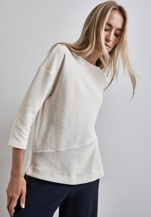 Top light beige a maniche 3/4 con texture a coste, scollatura a barca e design semplice senza motivi o decorazioni.