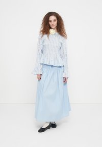 Φόρεμα σε ανοιχτό γαλάζιο με στρώσεις και υφασμάτινη υφή, με φαρδιά μανίκια, συνδυασμένο με μια αντίστοιχη ροή φούστα σε μπλε χρώμα. Μαύρα επίπεδα παπούτσια ολοκληρώνουν την εμφάνιση.