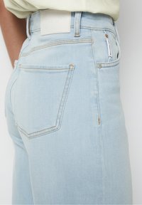 Světle modré denimové džíny s vysokým pasem, se bílou koženou nášivkou na zadní straně, jemným prošíváním a standartními zadními kapsami.