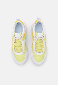 Limettengrüner und weißer Sneaker mit gelben Akzenten, ausgestattet mit abgerundeter Zehenpartie, strukturiertem Stoff und modernem Schnürdesign.