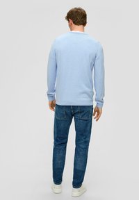 Lichtblauwe lange mouwen trui met een ronde halslijn, geribbelde manchetten en onderrand, gecombineerd met donkerblauwe jeans en witte sneakers.