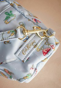 Šviesiai mėlynas siuvinėtas krepšys su spalvingais fantazijos raštais, auksinės spalvos detalėmis ir siuvinėta etiketė, ant kurios užrašyta "Cath Kidston".