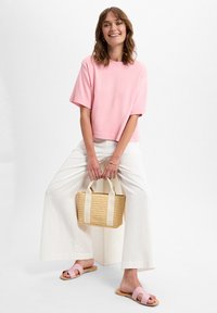 Helles rosa Baumwoll-T-Shirt mit kurzen Ärmeln, kombiniert mit weißen weit geschnittenen Hosen und einer geflochtenen Strohtasche. Dazu gehören blassrosa Rutschsandalen.