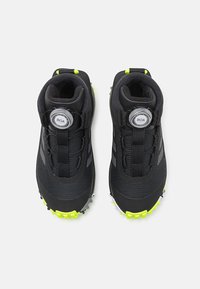 Czarne buty sportowe z teksturowaną cholewką, systemem sznurowania BOA i jasnymi żółtymi akcentami na podeszwie i pięcie. Posiadają podeszwę z kolcami dla lepszej przyczepności.