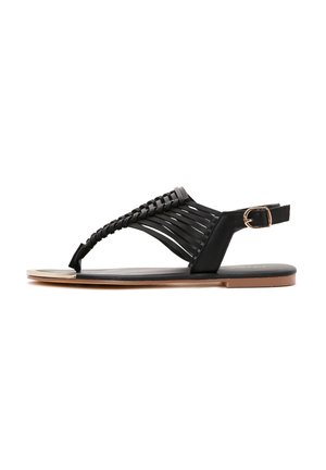 Black sandal featuring braided straps, an open toe design, a side buckle closure, and a flat sole with a metallic accent on the toe.