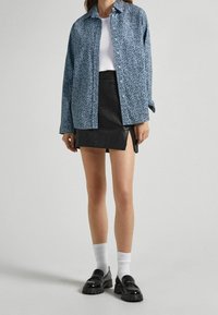Camisa de botones azul con estampado sobre una blusa blanca, combinada con una minifalda de cuero negro y unos zapatos de charol negros de suela gruesa con calcetines blancos.