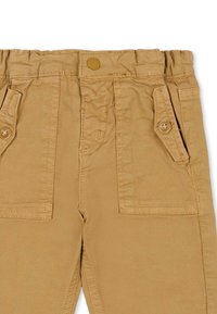 Beżowe spodnie cargo z elastycznym paskiem w talii, wyposażone w dwie przednie kieszenie z klapkami i guzikami, przeszycia oraz gładką teksturę tkaniny.