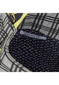 Harmaa ja musta ruutukuvioinen laukku keltaisella hihnalla, jonka sisäpuolella on pieniä hevoskenkiä esittävää kangasta ja jossa on etiketti, jossa lukee "CODELLO."