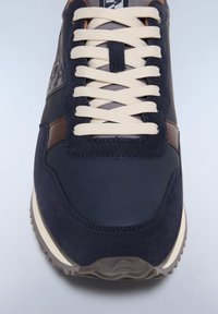Sneaker blu e marrone realizzata con una combinazione di materiali in suede e pelle, con lacci beige e suola texturizzata. Struttura solida e design moderno.
