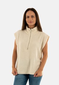 Top beige senza maniche con colletto alto e zip, caratterizzato da una texture a righe verticali e una vestibilità comoda. Accentato con un tessuto morbido.