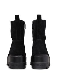 Botas de tobillo de ante negro con una suela de plataforma gruesa negra, que presentan cremalleras laterales y una marca a lo largo de la base. Acabado texturizado y diseño minimalista.