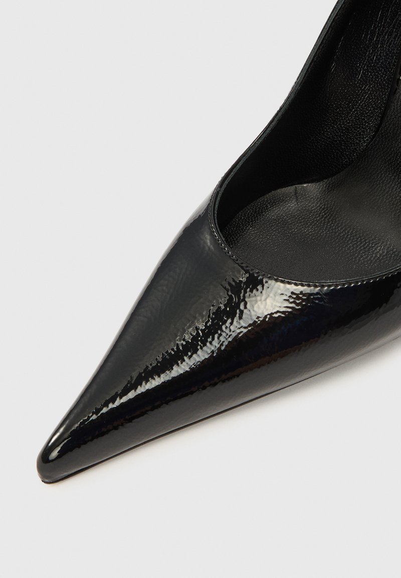 Black patent leather pointed-toe pump with a glossy finish and curved silhouette, featuring a smooth interior texture.