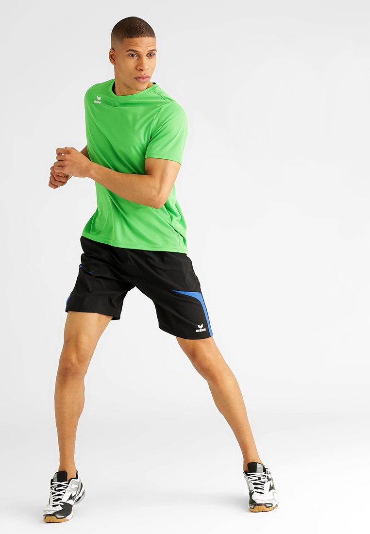 Groen sportshirt met korte mouwen en een ronde hals, gecombineerd met zwarte shorts met blauwe accenten; model in een hardlooppositie.