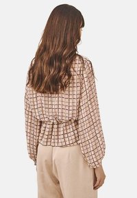 Blusa de manga larga en beige claro con un patrón de cuadros; presenta una cintura fruncida y un corte relajado. Tejido suave y ligero.