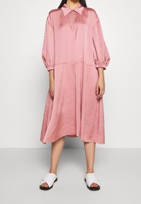 Pink satin dress with a pointed collar and balloon sleeves, featuring a zip closure and a flowy, knee-length silhouette. Worn with white sandals.