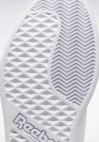 Semelle en caoutchouc blanc avec motifs texturés en losanges et en arêtes de poisson. Logo "Reebok" en gris le long du côté. Finition lisse avec motifs prononcés.