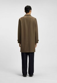 Brun uldfrakke med en skræddersyet pasform, der har en rygslids, sidelommer og enkle knapper, parret med mørk denim bukser.