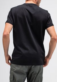 Schwarzes Baumwoll-T-Shirt mit kurzen Ärmeln, rundem Halsausschnitt und glatter Textur. Von hinten betrachtet, kombiniert mit grünen Cargo-Hosen.