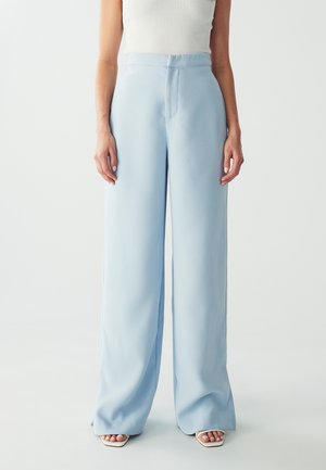 Lichtblauwe wijde broek met een gladde stof, hoge taille en een discrete voornaad. Gepaard met witte bandjeshakken.