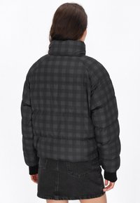 Černá kostkovaná péřová bunda s vysokým límcem, žebrovanými manžetami a boxy střihem. Materiál má hladkou strukturu s prošívaným designem.
