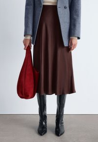 Brauner Satin-Midi-Rock, grauer strukturierten Blazer, rote Wildledertasche und schwarze geprägte kniehohe Stiefel. Glatte und figurbetonte Ästhetik.