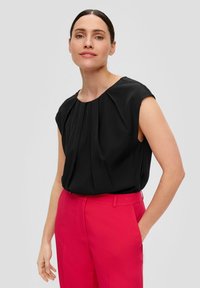 Top nero senza maniche con pieghe frontali e scollatura rotonda abbinato a pantaloni rosa a vita alta; tessuto morbido, design moderno.
