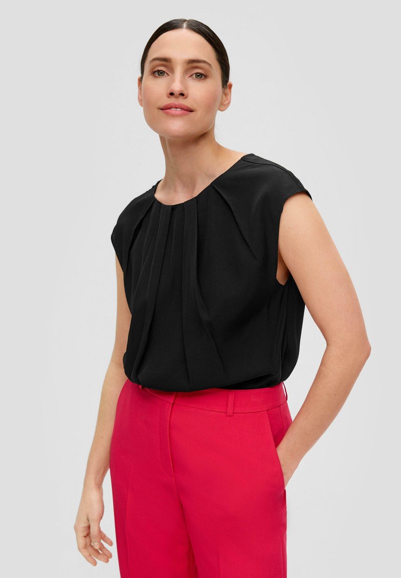 Top nero senza maniche con pieghe frontali e scollatura rotonda abbinato a pantaloni rosa a vita alta; tessuto morbido, design moderno.