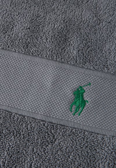 Γκρίζο υφασμάτινο ύφασμα με υφαντή ταινία που παρουσιάζει έναν μικρό πράσινο κεντημένο παίκτη πόλο πάνω σε άλογο.