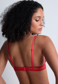 Soutien-gorge en dentelle rouge avec bretelles réglables, bande en maille transparente et fermeture par crochets. Présente des détails en dentelle complexes et une couleur vive.