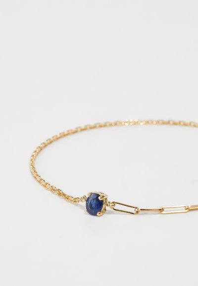 Gold chain bracelet featuring a blue oval gemstone set in a textured bezel. Chain has alternating link designs. Clean, minimalist aesthetic.