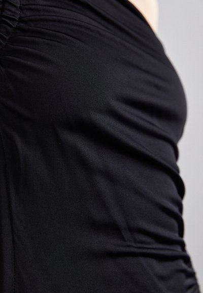 Svart, elastisk stoff topp med sammenkrøllede sidesømmer, glatt tekstur og en tettsittende design. Ideell for lagdeling eller som et selvstendig plagg.