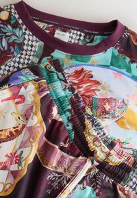 Bunt gemustertes Pyjama-Set mit einem Top mit lila Ausschnitt und passenden Hosen mit elastischem Bund, die festliche Motive und Texturen aufweisen.