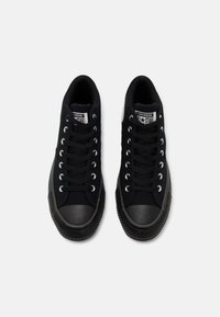 Svarta canvas-sneakers med gummitåhätta och texturerad sula. Har silverfärgade öglor och svarta snörningar, med en logotyp på sidan.