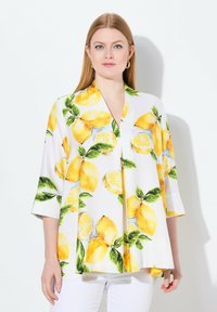 Blusa bianca con una vivace stampa di limoni. Maniche a campana e vestibilità comoda. Il materiale appare liscio, con dettagli di foglie verdi che decorano il tutto.