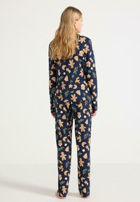 Ensemble de pyjama marin featuring un motif de biscuit en pain d'épice et sur le thème des fêtes. Fabriqué en tissu doux, avec un haut ajusté à manches longues et un pantalon assorti.