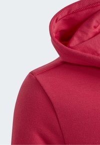 Red hoodie fabric close-up showing shoulder seam and inside of hood against a light gray background.