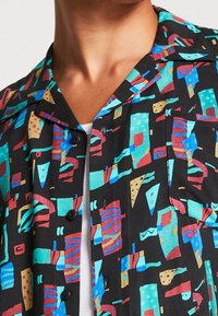 Korte mouwen shirt van lichtgewicht stof, met een zwarte achtergrond en kleurrijke abstracte geometrische patronen in blauw, rood, geel en groen.