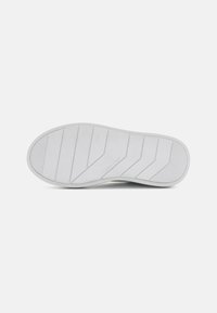 White rubber shoe sole with horizontal ridges and angled grooves for grip. Features Calvin Klein logo near the heel. Smooth texture.