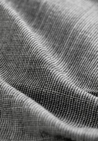 Gelaagd stof in tinten zwart en wit, met een houndstooth-patroon en een gladde, enigszins glanzende afwerking met subtiele glans.