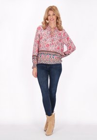 Bluză cu imprimeu floral, cu decolteu tip cheie, mâneci lungi și manșete elastice, asortată cu blugi de culoare albastru închis și bocanci scurți bej.